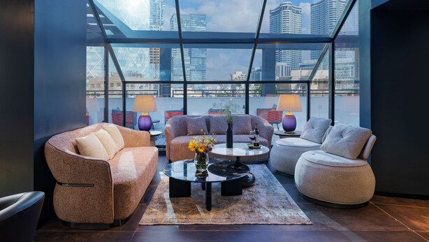 Eine moderne Lounge mit großem Fenster und Blick auf die Stadt, ausgestattet mit Sofas, einem Couchtisch und einer Vase mit Blumen.