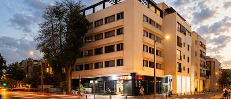 A multi-story building with a ground-level commercial space, a pedestrian crossing, and a street with moving traffic.