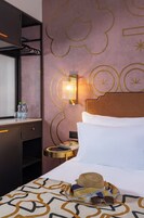 Una camera d'albergo con un letto, un comodino con una lampada, un armadio e una parete con decorazioni.