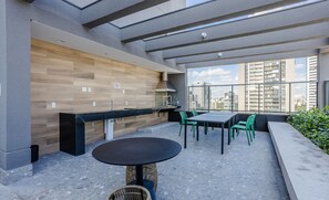 Um pátio moderno ao ar livre com área de refeições, cozinha integrada e vista para a paisagem urbana.