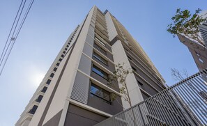A tall, modern building with a prominent vertical design, featuring multiple windows and a metal fence in the foreground.