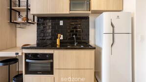 Eine kompakte Küche mit Holzausstattung, einer schwarzen Küchenzeile aus Fliesen, einer Mikrowelle, einem weißen Kühlschrank und einem eingebauten Backofen.