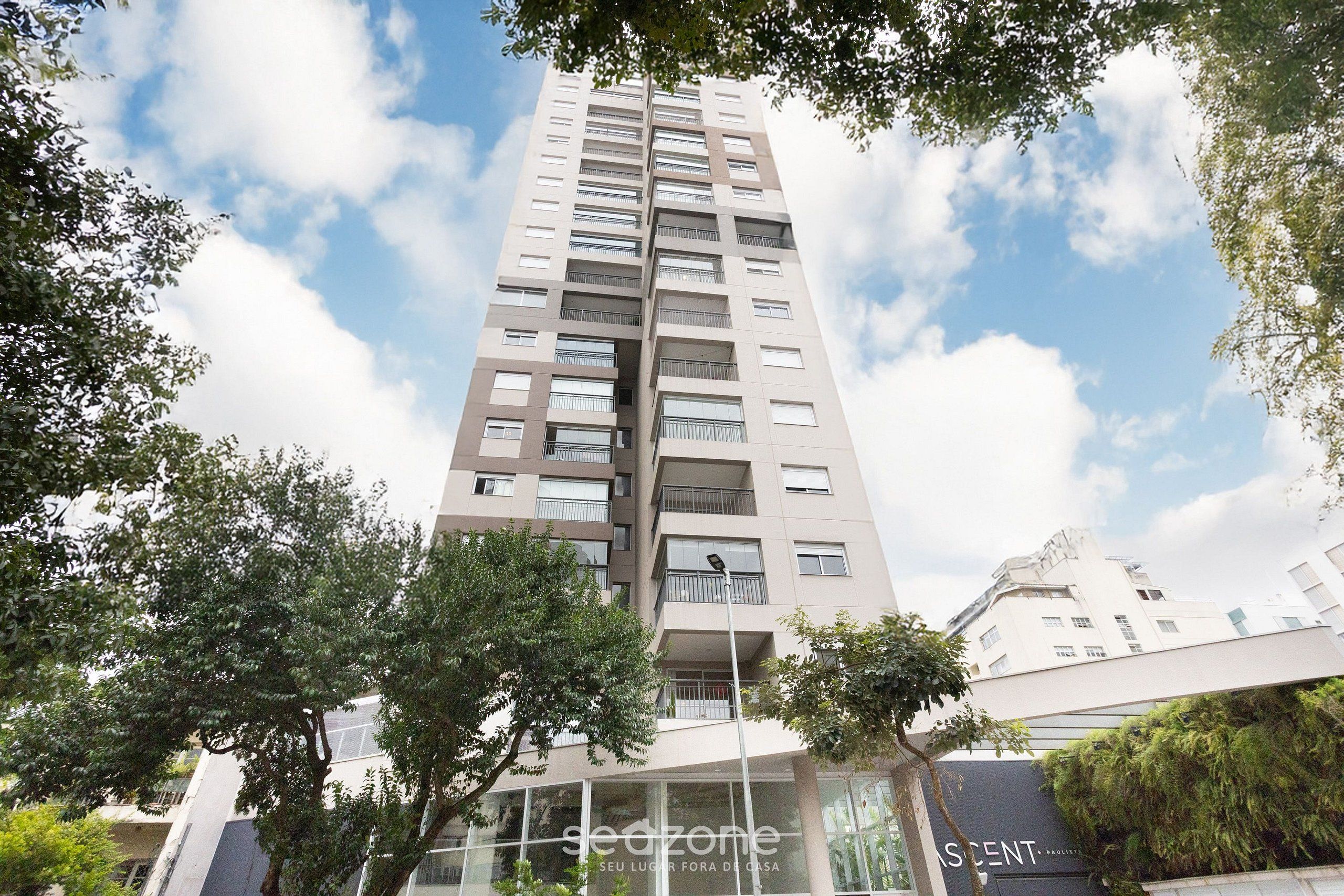 Un immeuble moderne de grande hauteur, doté de nombreux balcons et de grandes fenêtres, et entouré d’arbres.