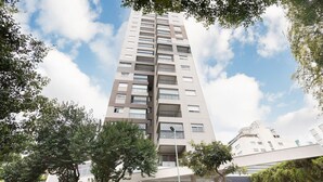 Ein modernes Hochhaus mit mehreren Balkonen und großen Fenstern, umgeben von Bäumen.