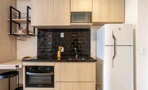 Une cuisine compacte avec des meubles en bois, un crédence en carreaux noirs, un four à micro-ondes, un réfrigérateur blanc et un four encastré.