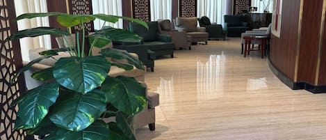 A spacious lobby with a large potted plant, multiple seating areas, and a reception desk.
