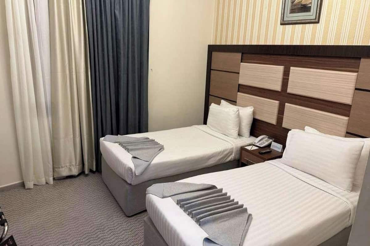 A hotel room with two beds, a nightstand, and a wall-mounted telephone.