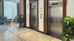Eine moderne Lobby mit drei Aufzügen, einem Café-Schild und einem Schild für die Toiletten.