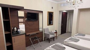 Ein Hotelzimmer mit Küchenzeile, Fernseher, Stuhl, Schreibtisch und zwei Betten.