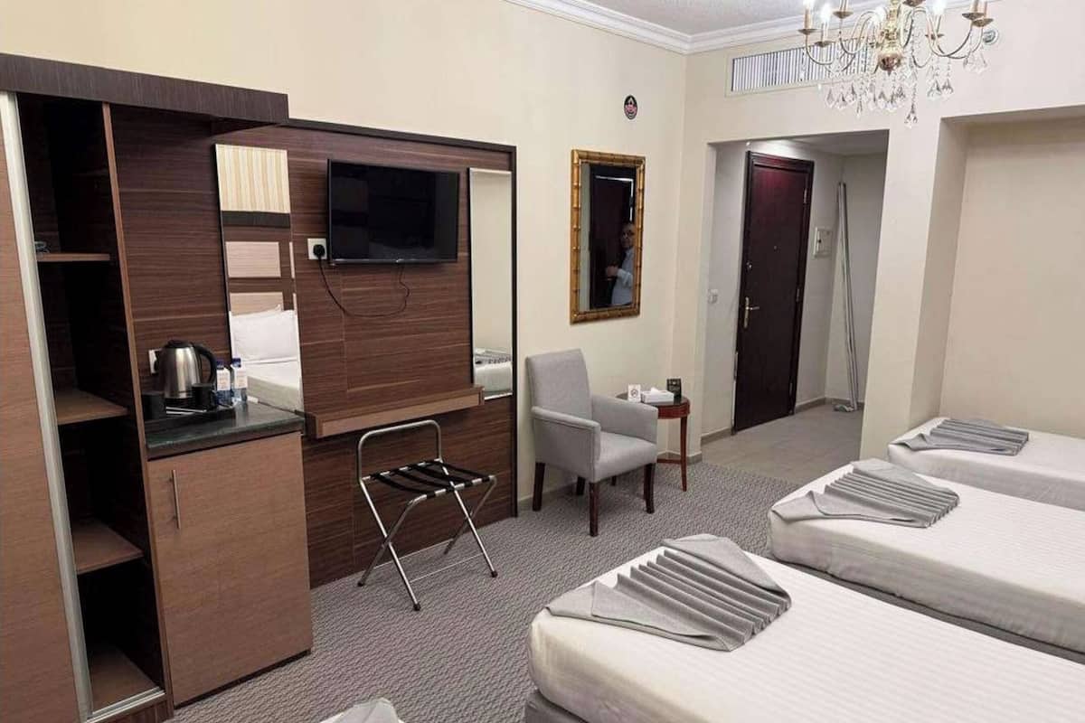 A hotel room with a kitchenette, a TV, a chair, a desk, and two beds.