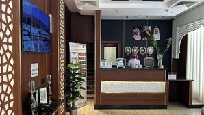 Ein Hotel-Empfangsbereich mit einem Holzbüro, einem großen Poster, einer Topfpflanze und einer dekorativen Wandverkleidung.