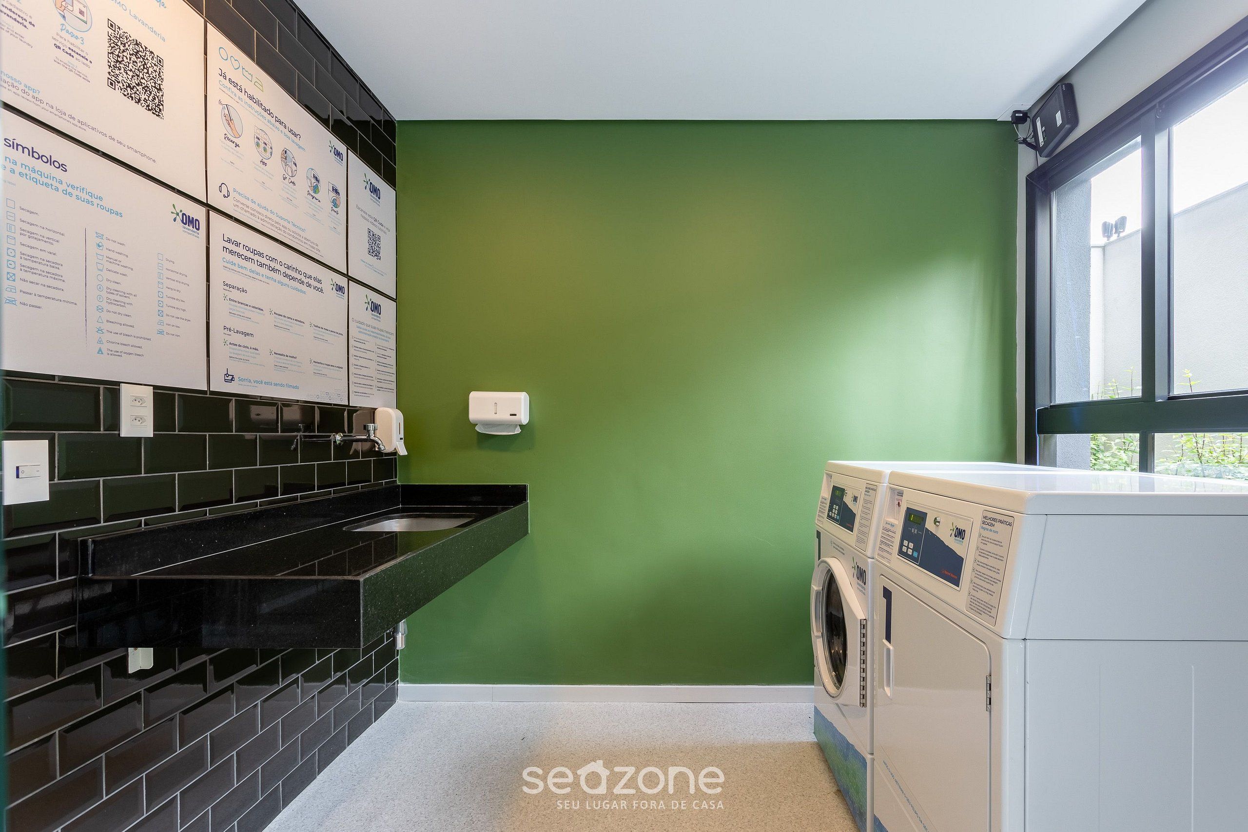 Une buanderie avec un mur vert, un comptoir recouvert de carreaux noirs et un lave-linge.