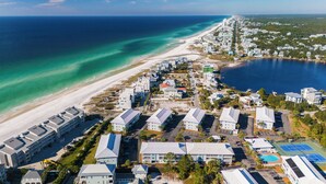 Vista aérea de un complejo turístico costero con propiedades frente a la playa, un puerto deportivo y una amplia zona de piscina.