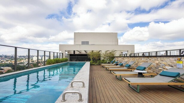 A rooftop pool with lounge chairs, a stone wall, and a view of the city. - Estúdio em SP perto do metrô | GBA908 (São Paulo)
