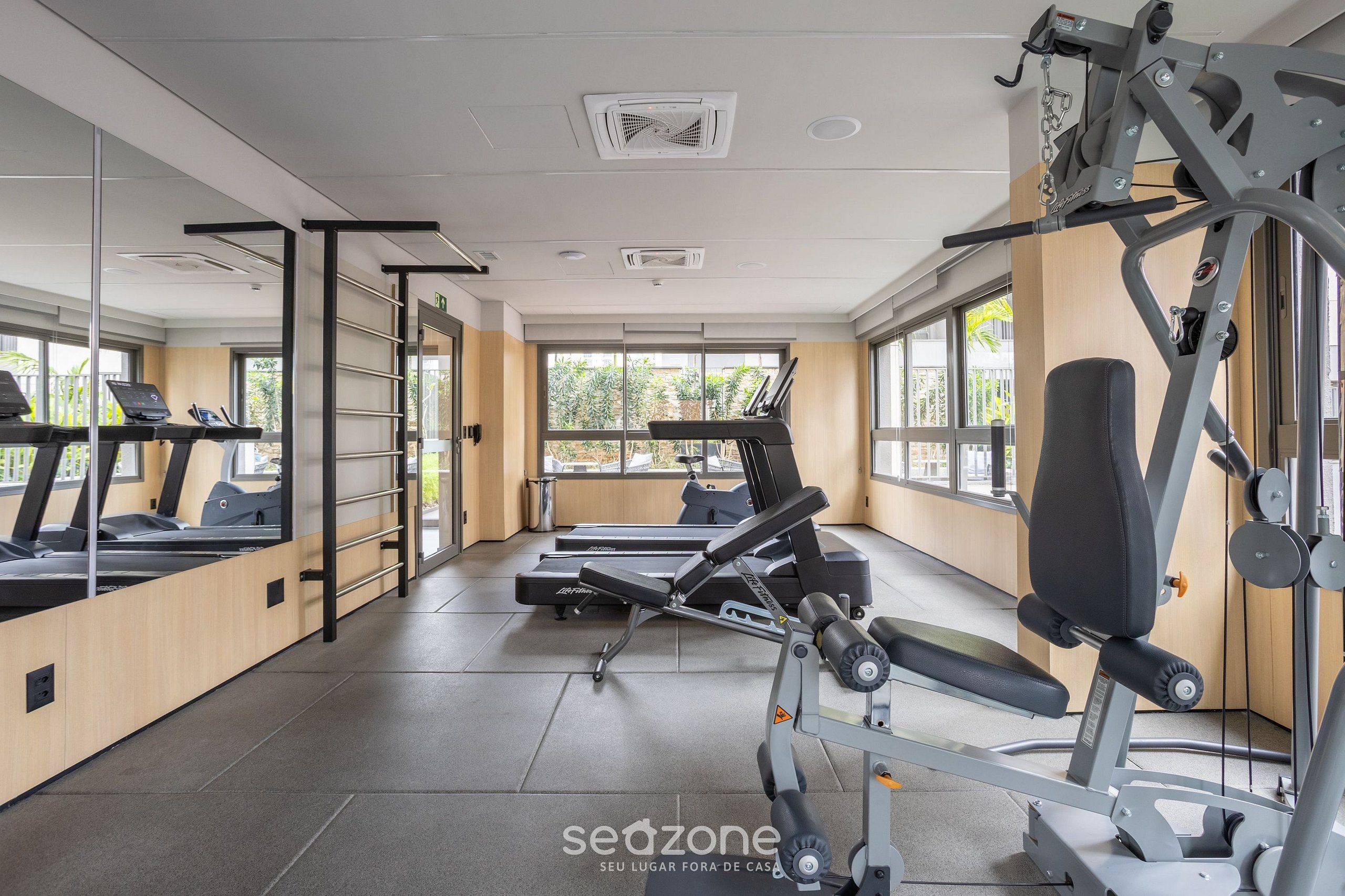 Een fitnessruimte met loopbanden, krachttrainingapparatuur en een spiegelwand.