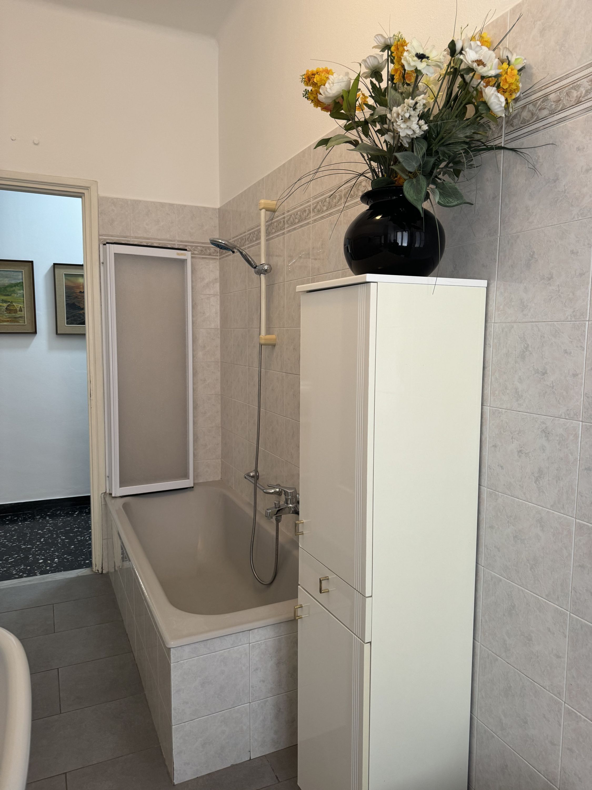 A bathroom with a bathtub, a shower, and a toilet. There is a vase with flowers on the wall.