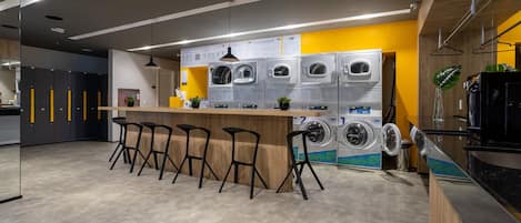 A modern laundry facility with multiple washing machines, bar stools, and a wooden counter.