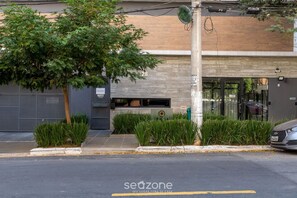 Un edificio moderno con un gran árbol en frente, un área de entrega y un coche estacionado en la calle.