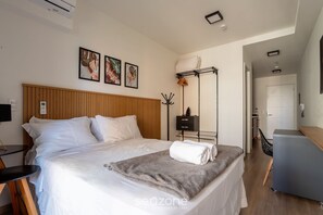 A neatly made bed with white linens, a grey throw blanket, and a folded towel on the side. There is a wooden headboard, a bedside table with a lamp, and a wall-mounted coat rack. - Modern Apartment in Vila Mariana Hma0305 (São Paulo)