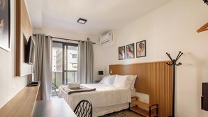 Habitación de hotel moderna con cama, escritorio, silla, televisor y balcón con vistas a edificios.