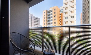 Un balcon avec une chaise noire et un petit tabouret, d’où l’on peut admirer une rangée d’immeubles d’appartements modernes.