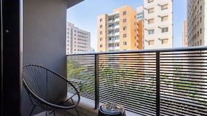 Un balcón con una silla negra y un taburete pequeño, con vistas a una hilera de edificios de apartamentos modernos.