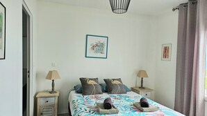 A bedroom with a bed, two nightstands, a hanging light fixture, and a window with curtains. - Superb Caiali Blue apartment (Les Trois-Îlets)