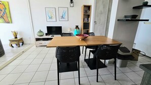 A dining area with a wooden table and black chairs, a TV, a bookshelf, and a decorative vase. - Superb Caiali Blue apartment (Les Trois-Îlets)