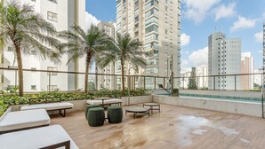 A rooftop terrace with seating, palm trees, and a view of surrounding high-rise buildings. - Beautiful Studio With Pool in Campo Belo Hmc0320 (São Paulo)