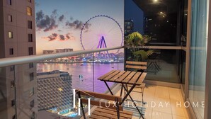 A balcony with a view of a Ferris wheel and a body of water, a wooden table, and a potted plant. - LUX  The Luxury Sunny JBR Beach Views 2  (Dubai)