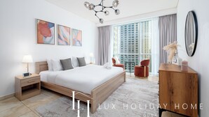 A modern hotel room with a large bed, a wooden nightstand, a desk, a chair, and a large window with a view of buildings. - LUX  The Luxury Sunny JBR Beach Views 2  (Dubai)