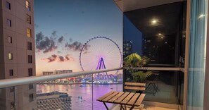 A balcony with a view of a Ferris wheel and a body of water, a wooden table, and a potted plant. - LUX  The Luxury Sunny JBR Beach Views 2  (Dubai)