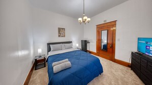 Een slaapkamer met een groot bed, een houten deur, een televisie en een tafeltje met een lamp.