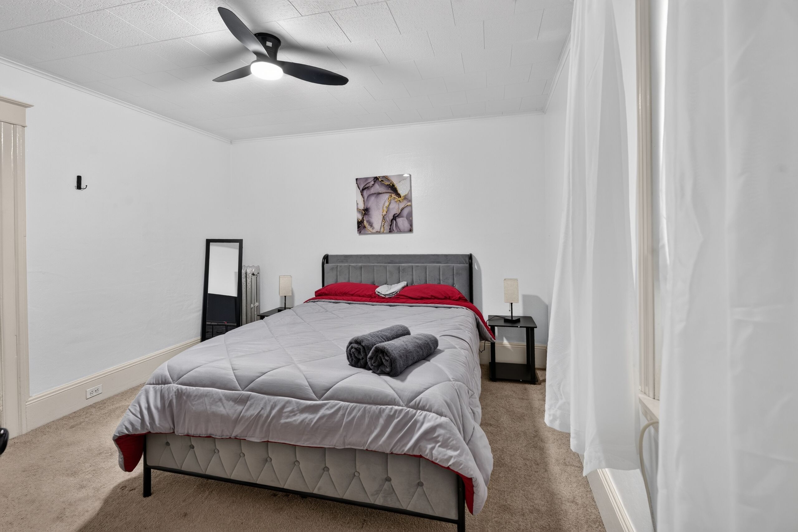 Una camera da letto con un letto, un ventilatore a soffitto, un comodino, una lampada e un quadro appeso al muro.