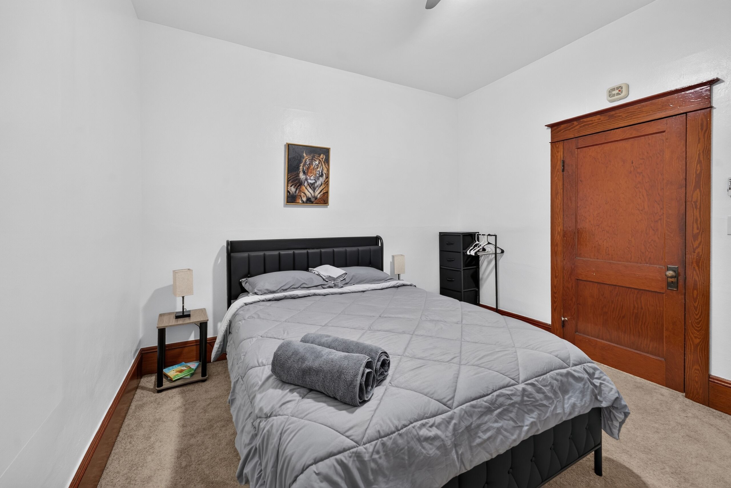 Une chambre à coucher avec un lit, une table de chevet, une lampe, une porte et un tableau au mur.