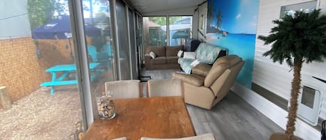 A modern living room with a wooden dining table, two chairs, a sofa, and a large window.
