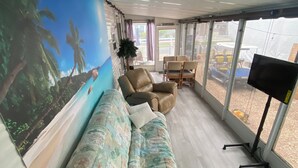 Een kamer met een bank, stoelen, een televisie en een muurschildering van een strand.