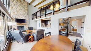 A spacious living area with a stone fireplace, modern furniture, and a large dining table. - On Lake, WOW Views, Big Deck! Walk to Amp, Events, Parks, Marina, Tiki Bar (Dillon)