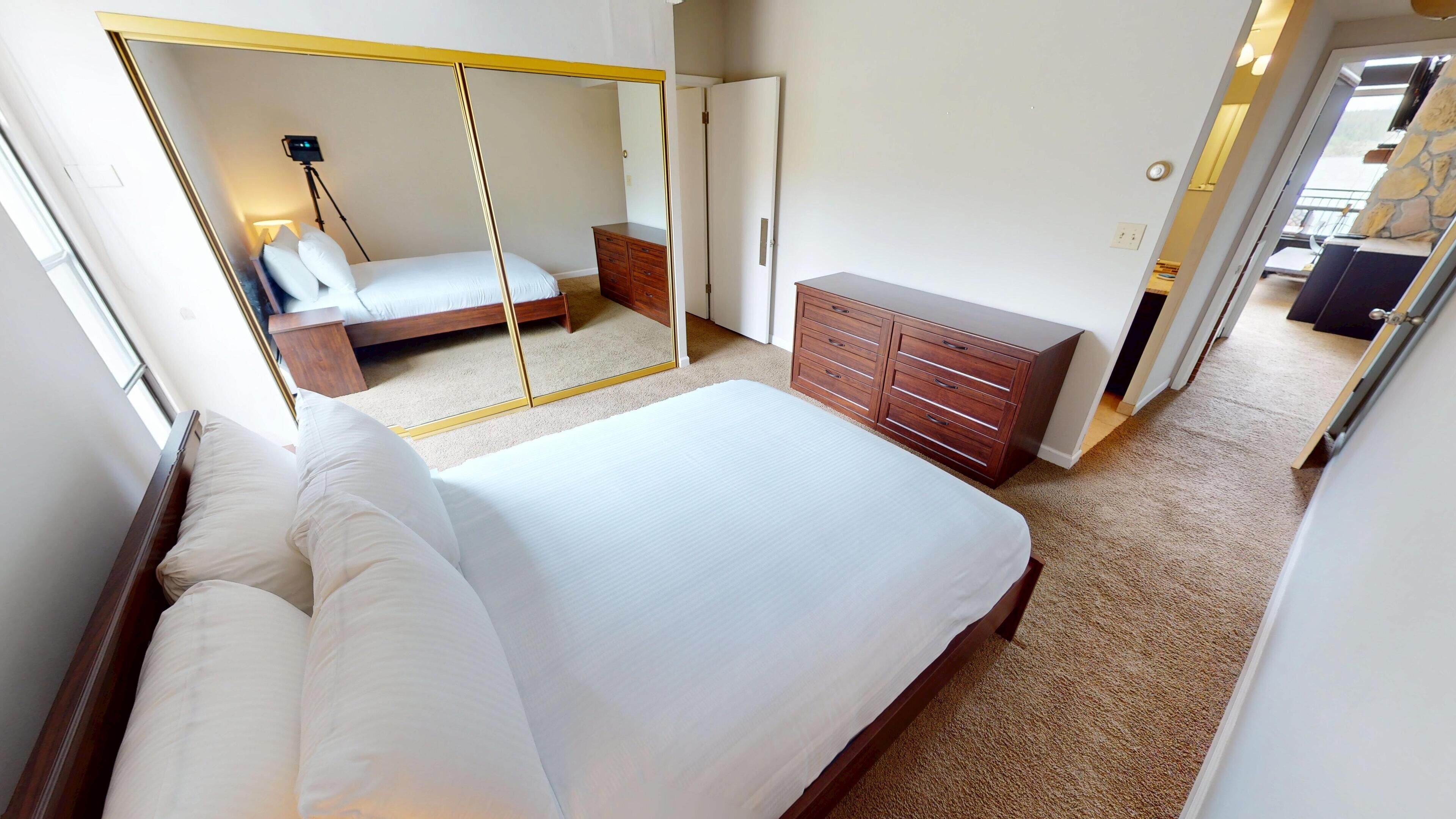 A bedroom with a bed, a dresser, a mirror, and a door leading to another room.