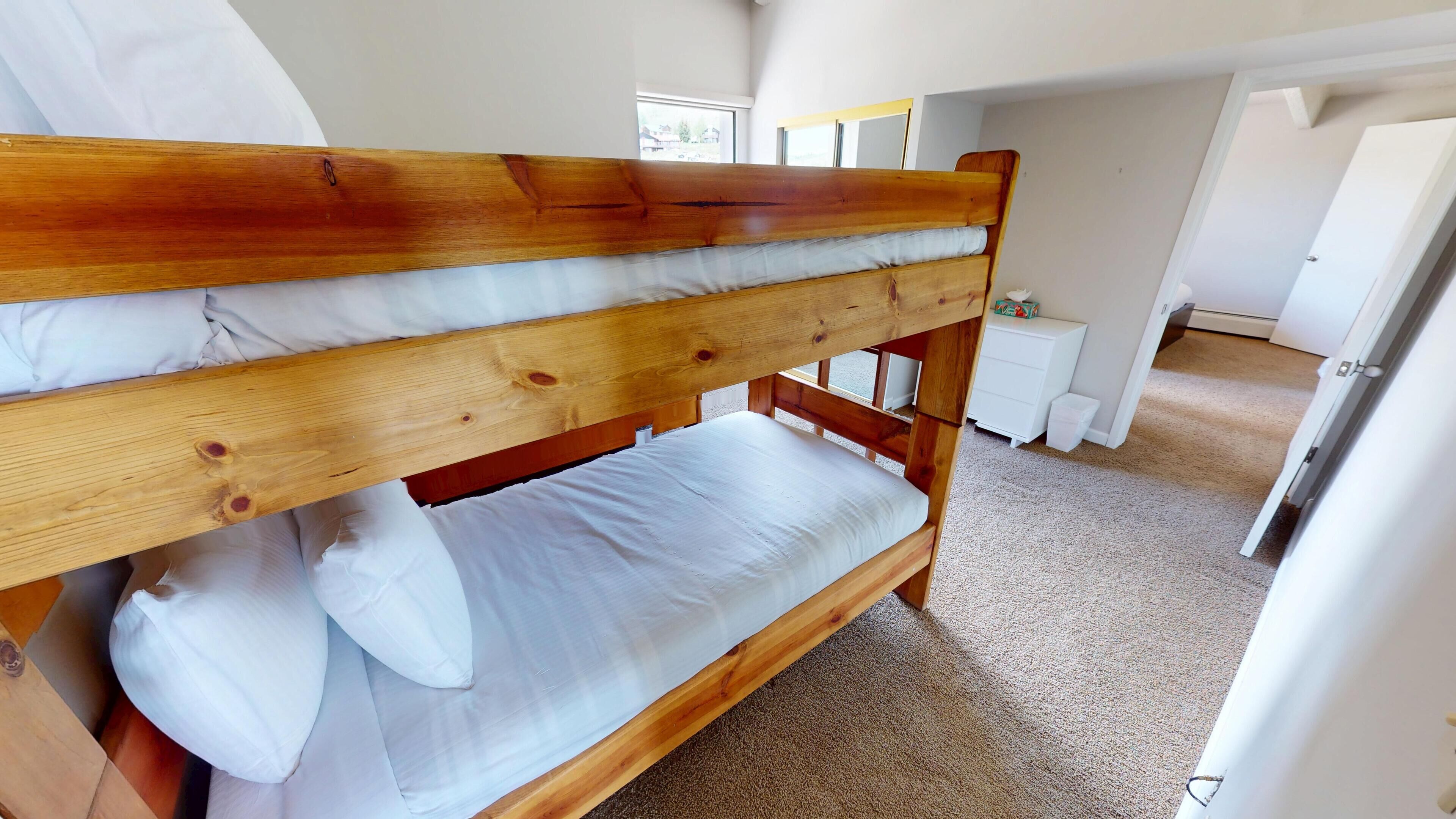 A bunk bed with white bedding in a room with carpeted floors and white walls.