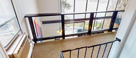 A balcony with a view of a lake and mountains, a metal railing, and a carpeted floor.