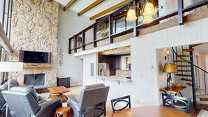 A spacious living area with a stone wall, a fireplace, a flat-screen TV, and a dining table with chairs. - On Lake, WOW Views, Big Deck! Walk to Amp, Events, Parks, Marina, Tiki Bar (Dillon)