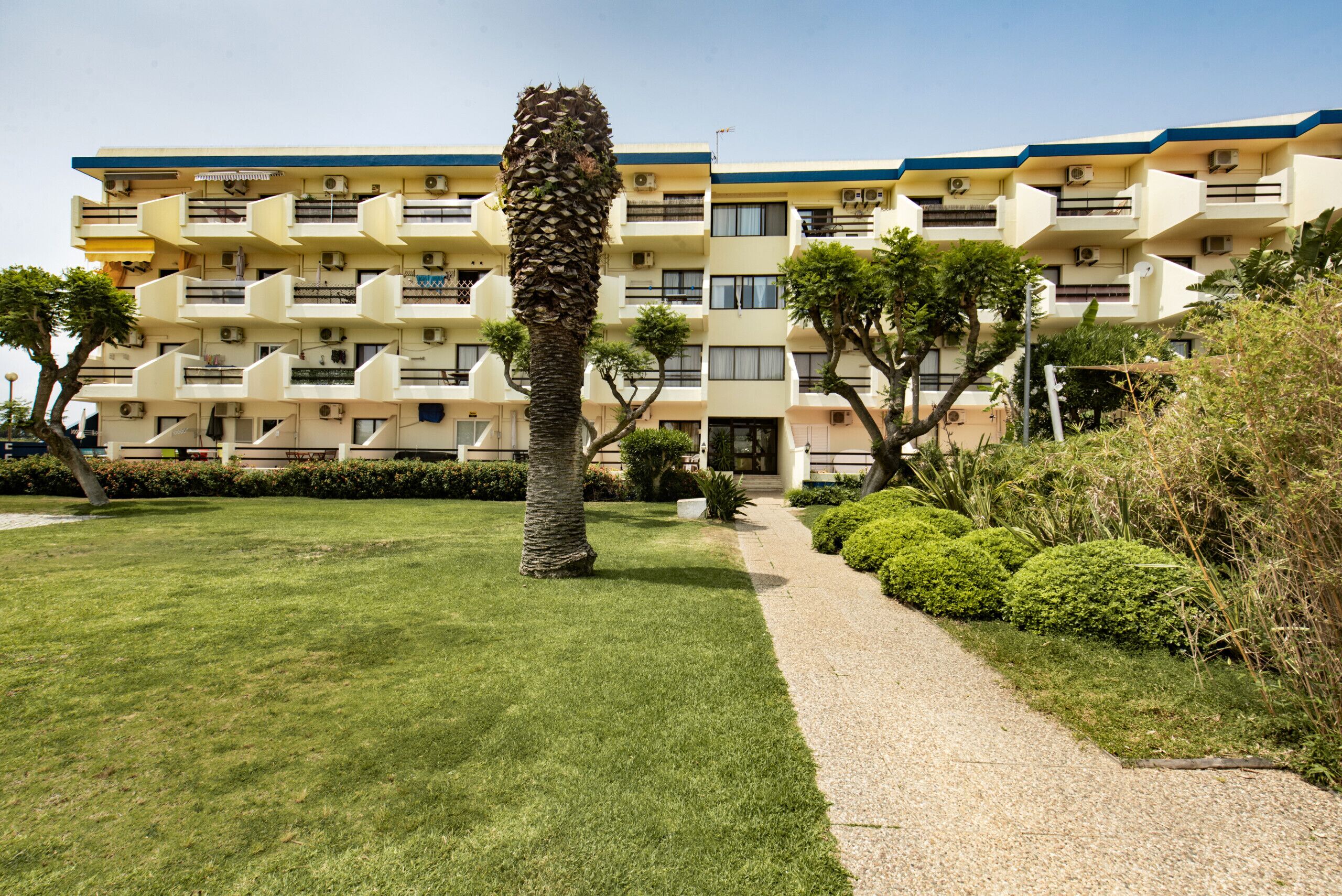 A multi-story building with balconies, a well-maintained lawn, and a pathway leading to the entrance.