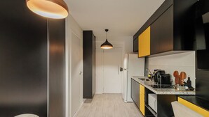 A modern kitchen with a central island, black and yellow cabinets, a refrigerator, and a pendant light.