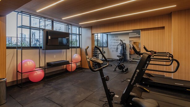 A modern gym with exercise equipment, a TV on a wall, and large windows.