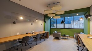 A modern meeting room with a long wooden table, several chairs, a small sofa, and pendant lighting.