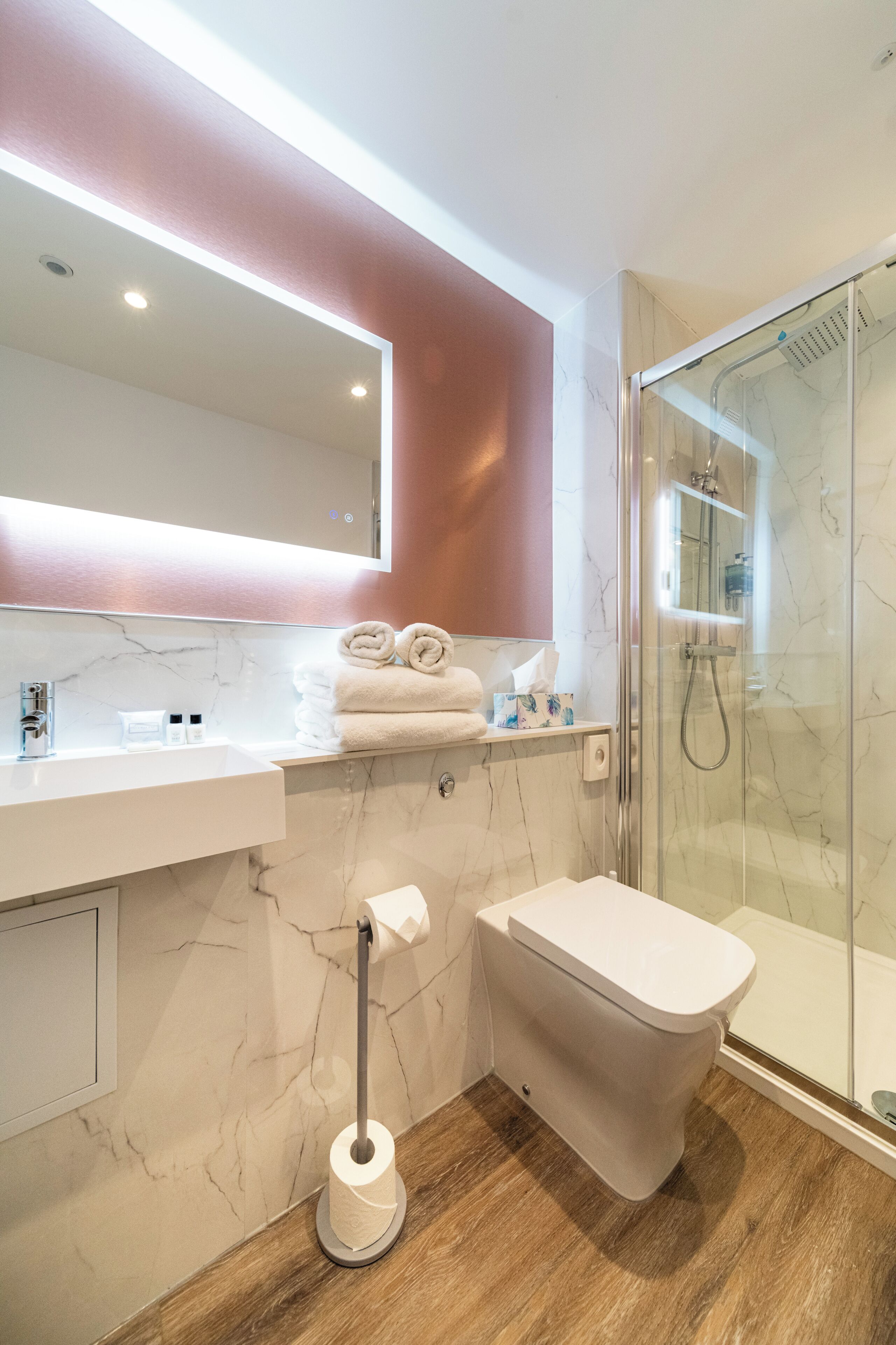 A modern bathroom with a marble sink, a toilet, a glass shower enclosure, and a towel rack.