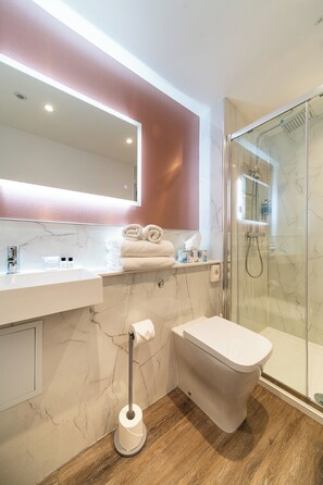 A modern bathroom with a marble sink, a toilet, a glass shower enclosure, and a towel rack.