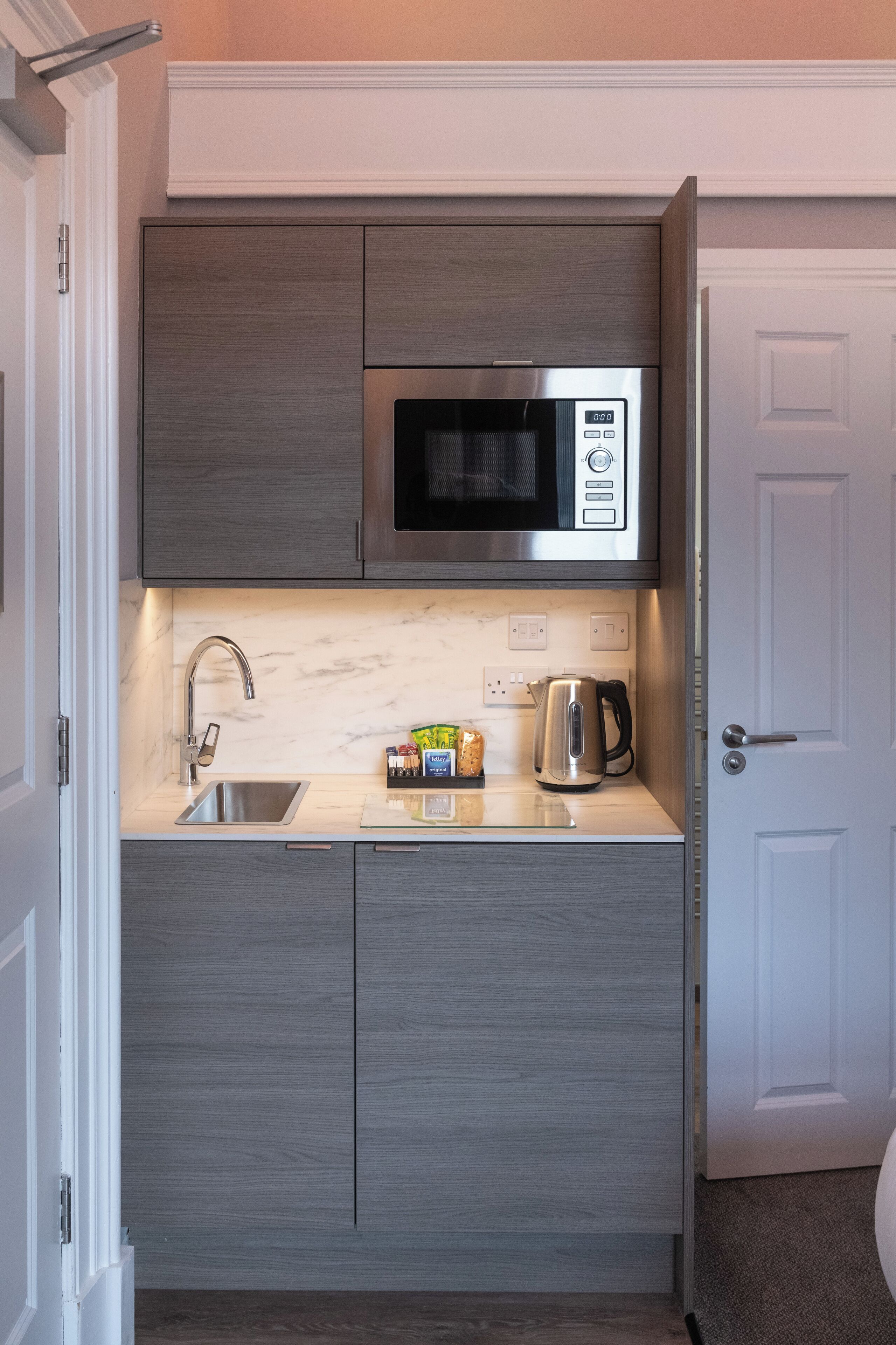 Una cocina compacta equipada con microondas, pileta de acero inoxidable y tetera.