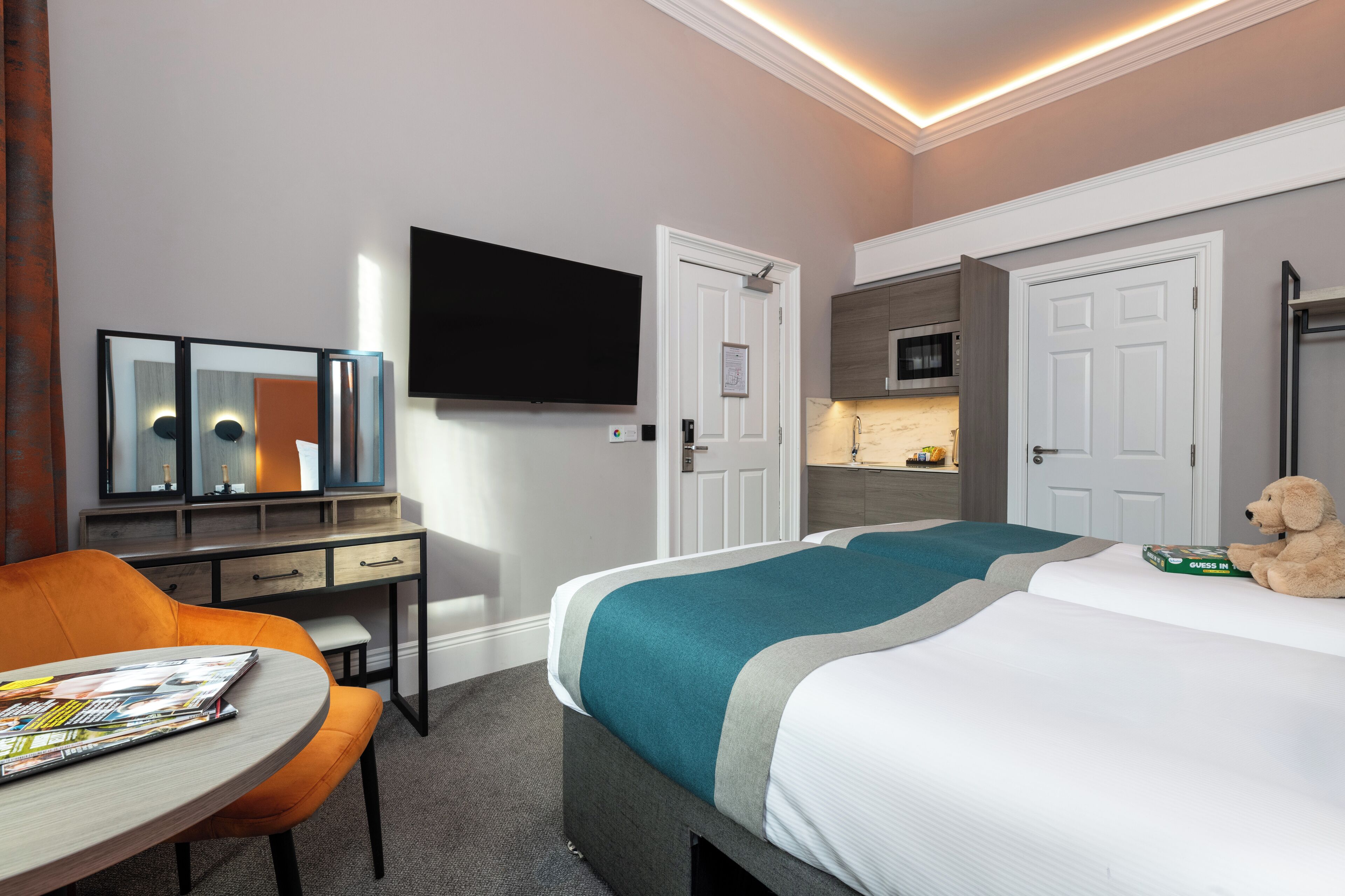 A hotel room with a bed, a desk, a chair, a television, and a teddy bear.